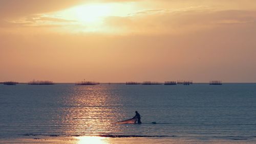 Silhouette man in sea against sky during sunset