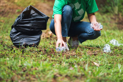 A female activist picking up garbage plastic bottles into a plastic bag in the park for recycling