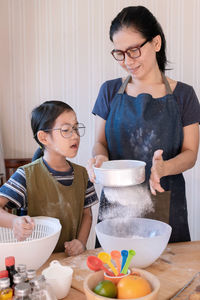 Mother teaches daughter how to sift the flour