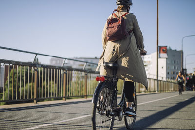 Rear view of businesswoman with backpack riding bicycle on lane