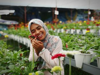 Smiling young woman holding flower in greenhouse