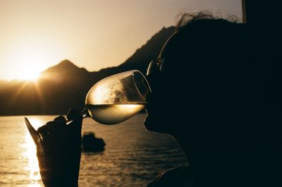 Close-up of silhouette woman drinking wine during sunset