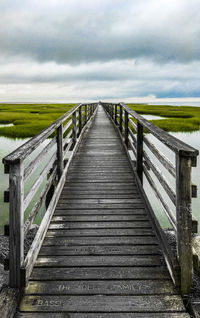 Wooden footbridge leading to pier against sky