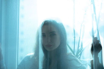 Portrait of a young woman looking through window