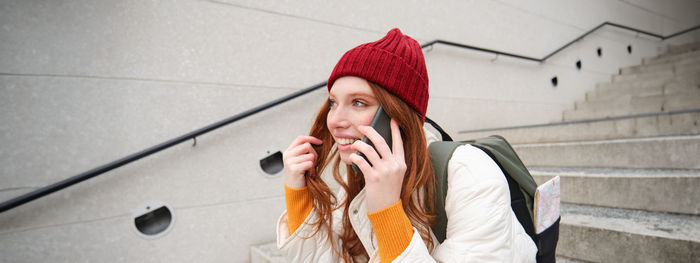 Young woman using mobile phone while standing against wall