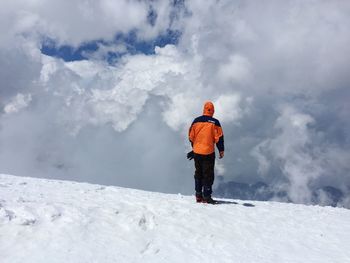 Rear view of man standing on snowcapped mountain against cloudy sky