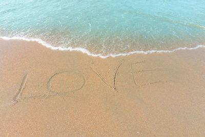 Love word hand writing letter on brown sand beach washed by small wave of blue water in the sea