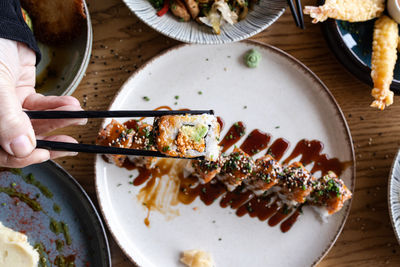 Hand lifting a sushi roll with chopsticks from a plate of japanese food