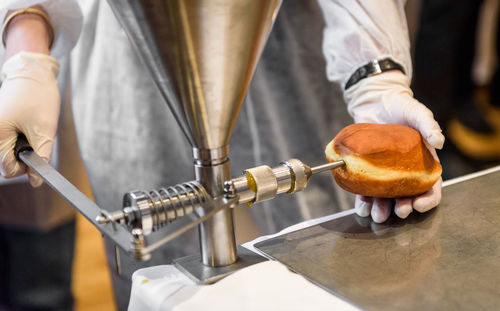 Midsection of man using appliance while filling donut at factory