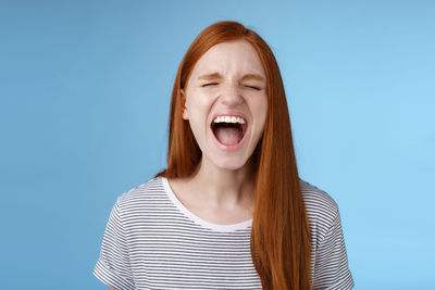 Angry young woman against blue background