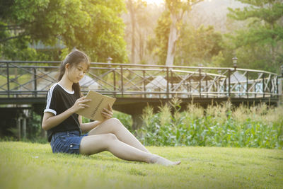 Woman reading book while sitting on footbridge at park