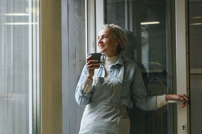 Smiling craftswoman holding coffee cup at doorway in workshop