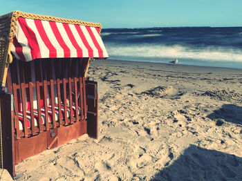 Hooded beach chair on shore against sky