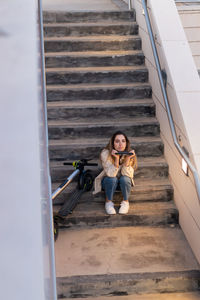 Woman sitting in concrete leaning on a black tablet with electric scooter next to her to return home