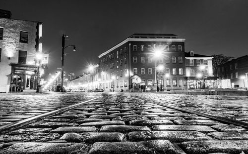 Illuminated street amidst buildings against sky at night