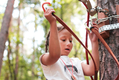 Low angle view of girl attaching safety harness on rope in forest