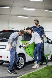 Male friends with woman charging electric car at gas station