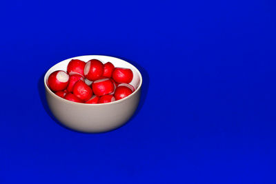High angle view of radishes in bowl on blue background