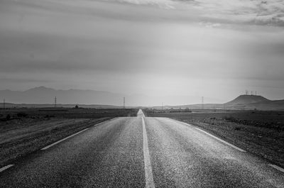 Empty road amidst field against sky