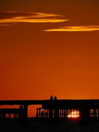 Silhouette people by sea against orange sky