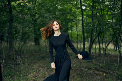 Portrait of young woman standing against trees