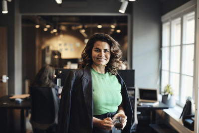 Portrait of happy female entrepreneur with tea cup standing at office