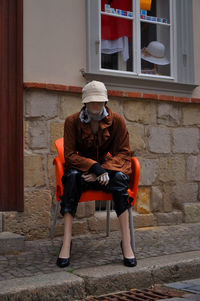 Full length of man sitting on seat against wall