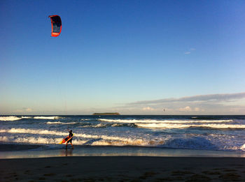 Parachuting on beach against clear blue sky
