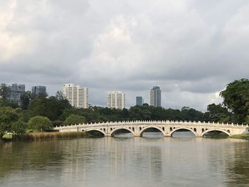 Arch bridge over river by buildings against sky in city