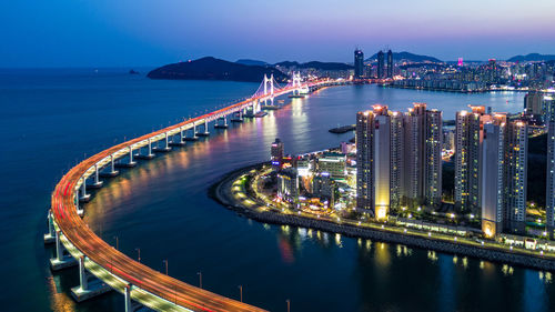 High angle view of illuminated city by sea against sky