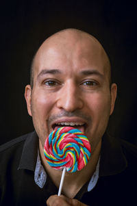 Close-up portrait of smiling man licking lollipop against black background