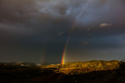 Scenic view of rainbow over mountain against dramatic sky