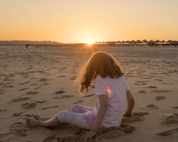 Rear view of woman standing at beach during sunset