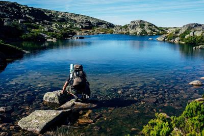 Hiker sitting on rock at lakeshore against mountains