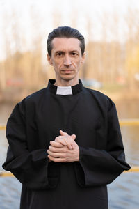 Portrait of priest standing against trees