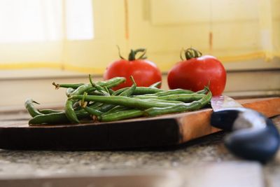 Green chilies and tomatoes on cutting board by knife in kitchen