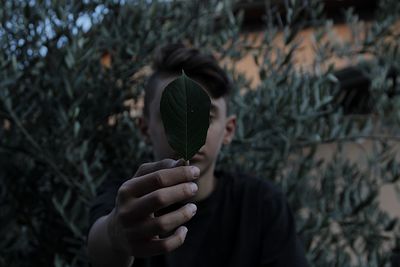 Teenage boy holding leaf against face