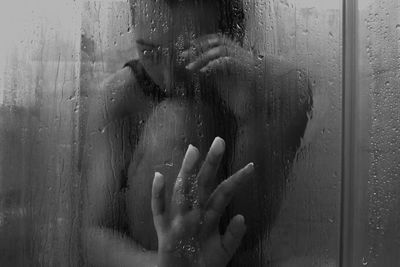 Naked woman taking bath seen through wet glass at home