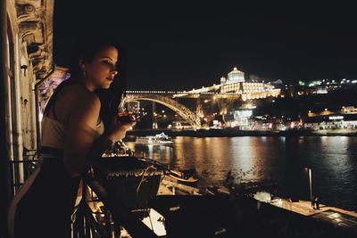 Young woman with illuminated cityscape in background at night