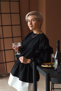 Fashion woman short blond hair in vintage black and white dress holding elegant glass for cocktail