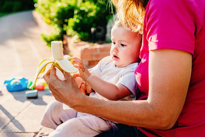 Midsection of mother feeding banana to baby at back yard