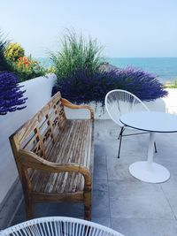 Empty chairs and table by sea against sky