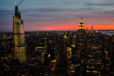 Illuminated buildings in city against cloudy sky