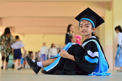 Portrait of girl wearing graduation gown and mortarboard while sitting on floor