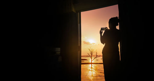 Rear view of woman taking picture of sunset