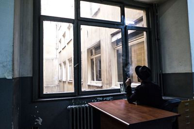 Rear view of man smoking while sitting on table by window