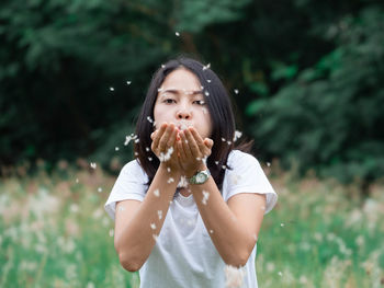 Portrait of young woman blowing dandelions on field