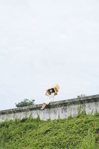 Full length of woman sitting on wall against sky