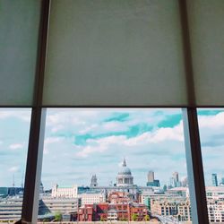 View of cityscape against cloudy sky seen through window