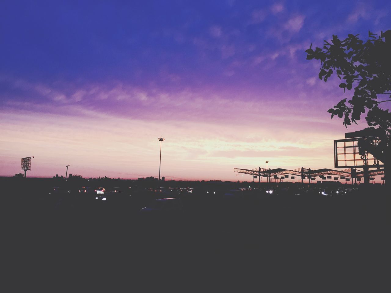 sunset, silhouette, sky, building exterior, architecture, built structure, dusk, cloud - sky, city, tree, cloud, outdoors, street light, no people, orange color, low angle view, transportation, illuminated, dark, nature